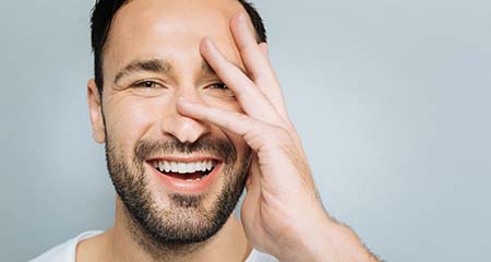 Man smiles with hand on face.