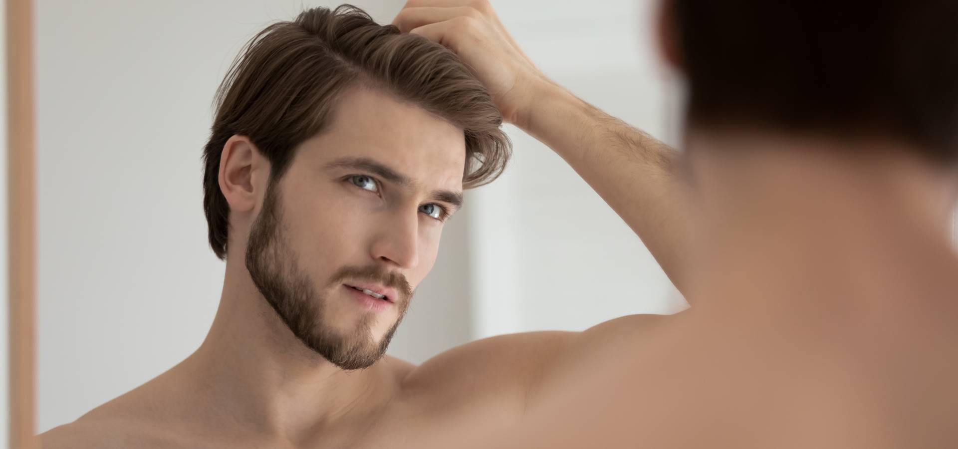 Man looks in mirror and touch hair.